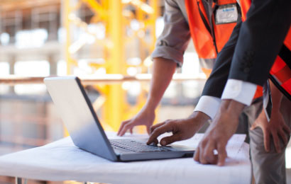 Zwei Menschen stehen auf einer Baustelle vor einem Laptop.